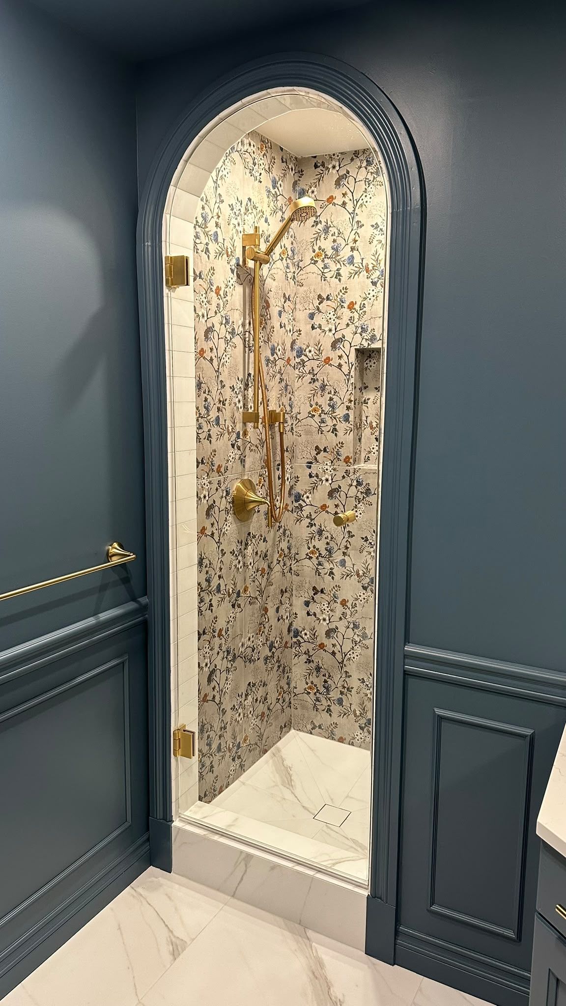 Arched shower framed by blue walls with floral tile and brass fittings