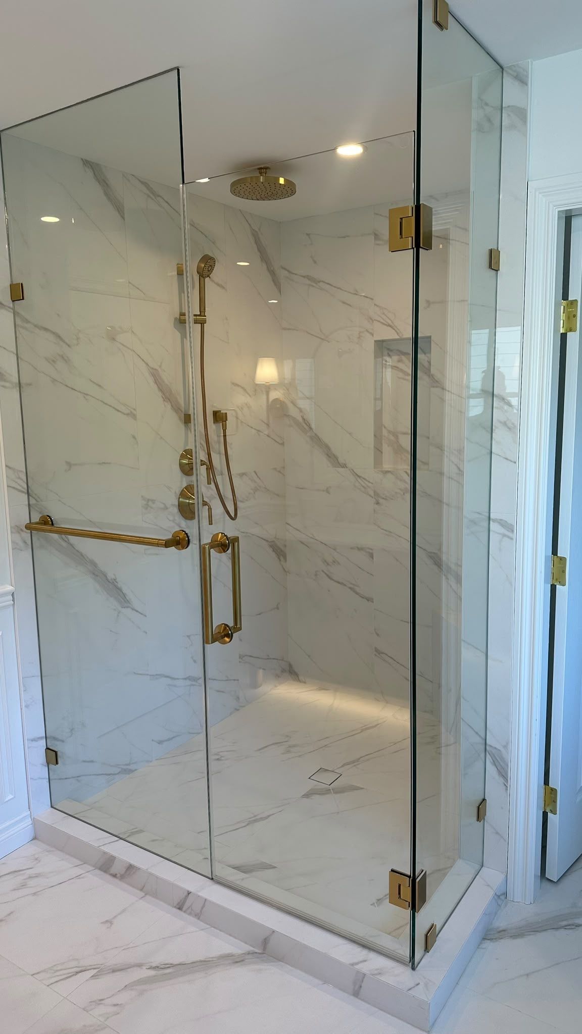 Glass-enclosed shower with pale tile and brushed brass fixtures