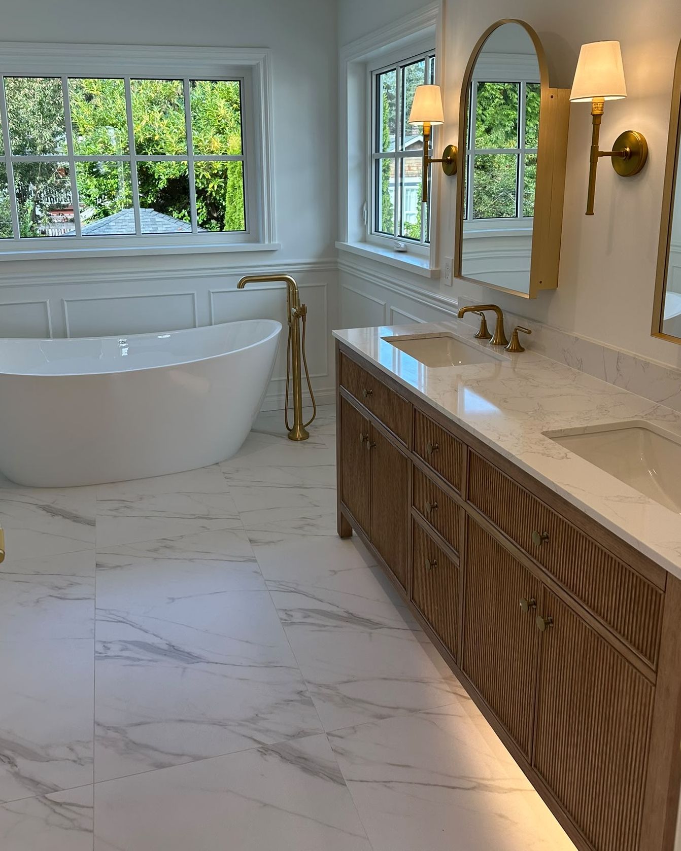 Freestanding bath beside a fluted wood vanity with brass fittings