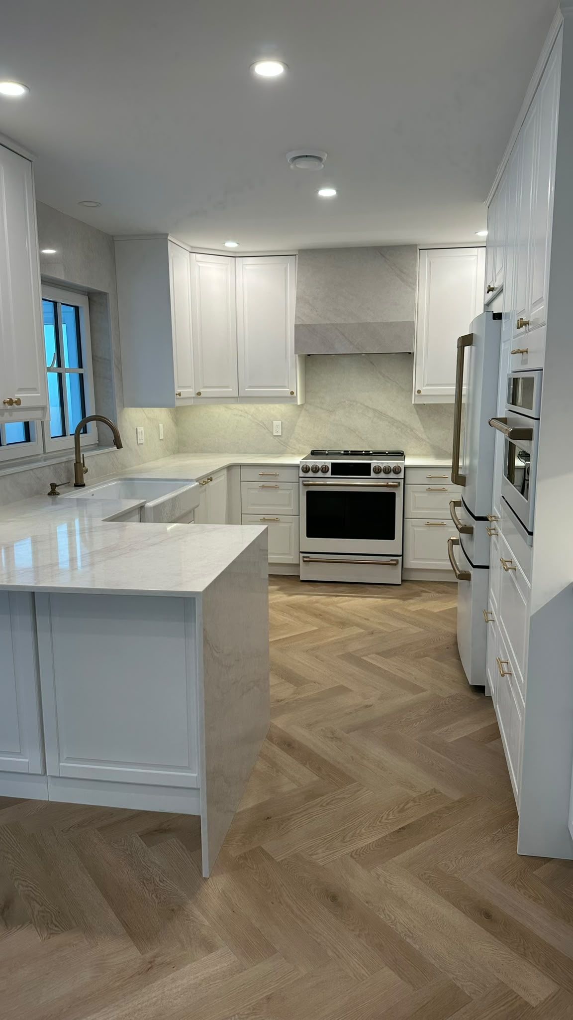 White kitchen with a waterfall peninsula, integrated hood and brass hardware