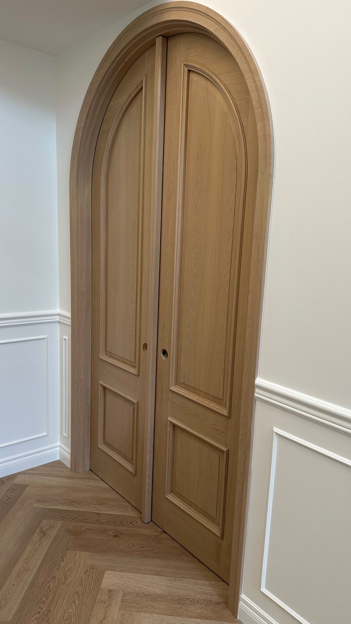 Arched oak double doors surrounded by curved white casing